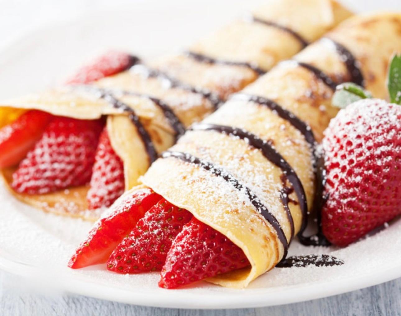 Delicious crepes with Strawberry pieces, chocolate syrup and powdered sugar