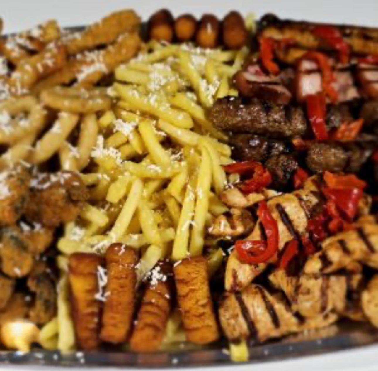 A platter of grilled meats, chicken, beef, and fries on top, with red pepper. 
