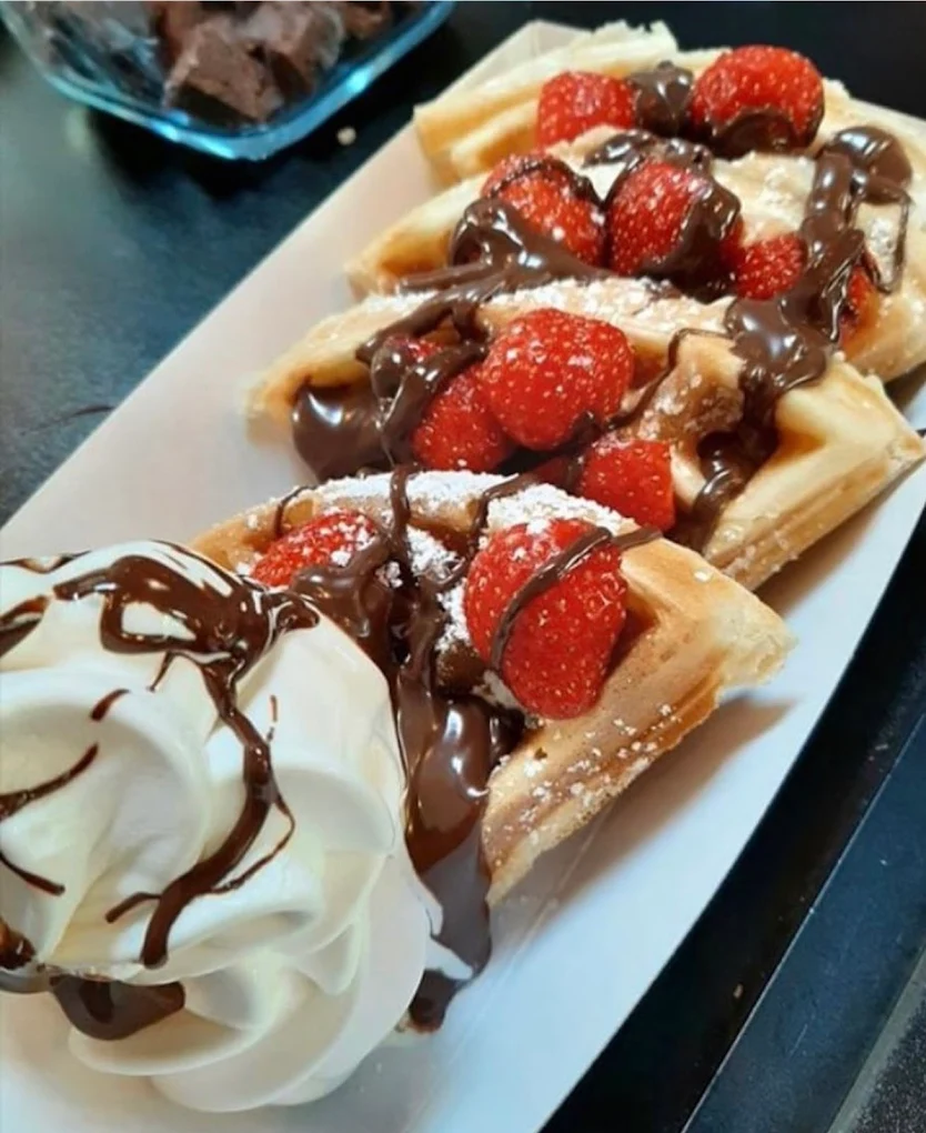 Golden Belgian waffle topped with fresh strawberries, chocolate sauce and whipped cream, served on a white plate.