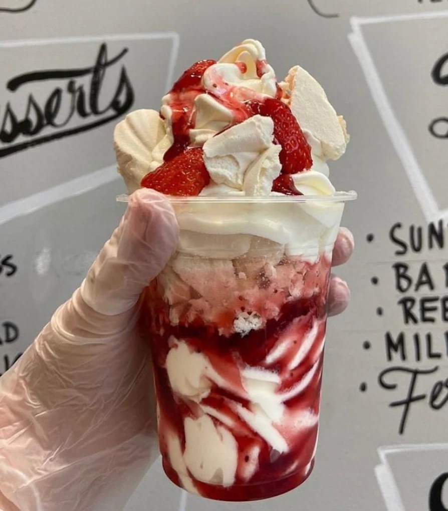 Layered strawberry sundae with vanilla ice cream, fresh strawberries, strawberry sauce and meringue pieces, served in a clear cup.