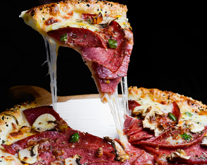 A close-up of a hand lifting a steaming slice of gourmet pepperoni and mushroom pizza, featuring a dramatic cheese pull against a dark, moody background. ready for order.