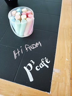 Tables with chalkboard paint for all to colour on. It says Hi from P³ Café in this image.